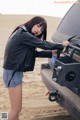 A woman in a black leather jacket and denim shorts standing next to a car.