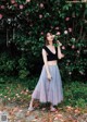 A woman standing in front of a bush of flowers.