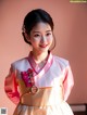 A woman in a pink and white hanbok poses for a picture.