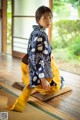 A woman in a blue and yellow kimono sitting on a wooden floor.