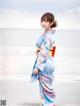 A woman in a blue kimono standing on the beach.