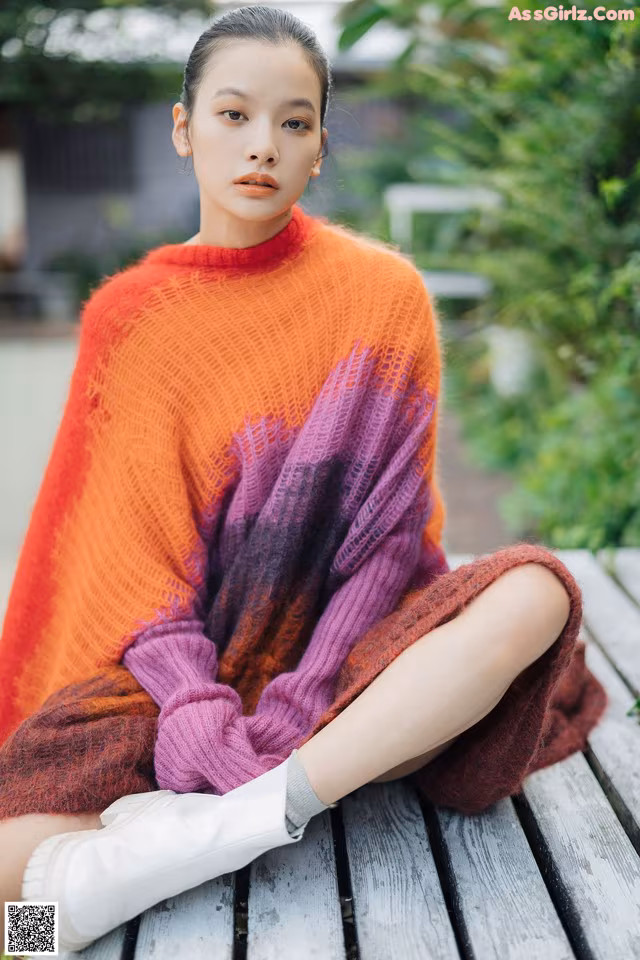 A woman sitting on a wooden bench wearing a colorful sweater.
