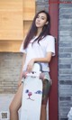 A woman holding a skateboard leaning against a brick wall.