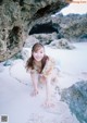 A young woman crouching down on the sand in front of a rock.