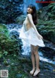 A woman in a white dress standing in front of a waterfall.