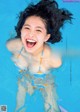 A young woman in a blue swimming pool with her hair in the air.