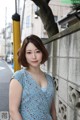 A woman in a blue dress leaning against a wall.