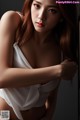 A woman in a white top leaning against a wall.