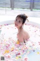 A woman sitting in a bathtub filled with flowers.